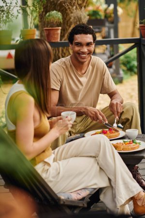 Ein gemischtrassiges Paar genießt ein Picknick auf einer Bank und teilt eine gemeinsame Mahlzeit in einem Moment romantischer Verbindung.