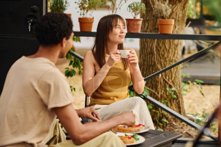 Foto de Un hombre y una mujer disfrutan de un momento tranquilo en un banco, saboreando tazas de café en compañía de los demás. - Imagen libre de derechos