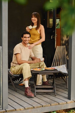 An interracial couple sits together on a porch, enjoying a peaceful moment in each others company.