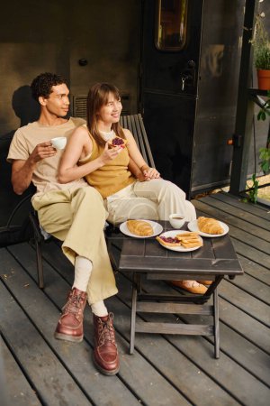 An interracial man and woman peacefully sitting together on a porch, enjoying each others company in a tranquil setting.