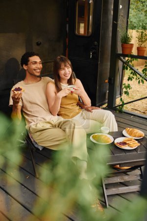 Téléchargez les photos : Un couple interracial s'assoit ensemble sur une véranda confortable, profitant d'un moment de détente paisible. - en image libre de droit