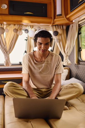 A man of mixed race sitting comfortably on a couch, focused on his laptop screen.