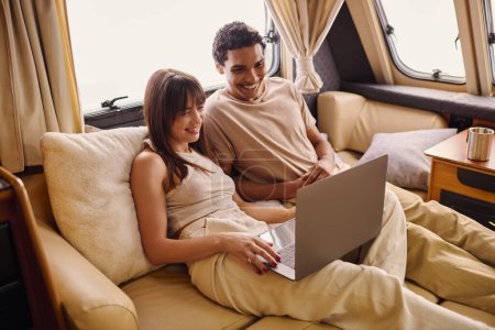 Foto de Un hombre y una mujer de diferentes etnias se sientan en un sofá, absortos en el uso de un portátil juntos. - Imagen libre de derechos