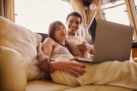 Photo for A man and woman relax on a couch, engrossed in a laptop screen. - Royalty Free Image