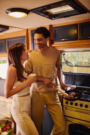 Foto de Una pareja interracial se encuentra lado a lado frente a una estufa, participando en una experiencia culinaria compartida. - Imagen libre de derechos