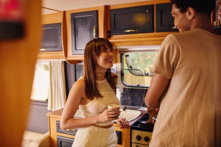 Una mujer con estilo en un vestido blanco de pie junto a un hombre en una cocina, compartiendo un momento en su elegante entorno.
