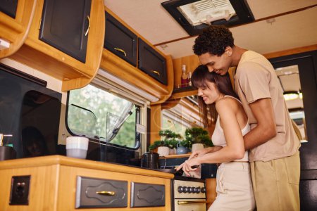 Una pareja interracial se encuentra en una acogedora cocina, compartiendo un momento de intimidad y asociación mientras prepara una comida.
