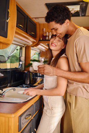 Téléchargez les photos : Un couple interracial se tient côte à côte dans leur cuisine, engageant la conversation à côté de l'évier. - en image libre de droit