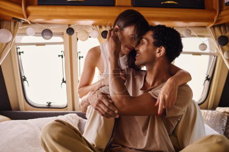 Ein Mann und eine Frau verschiedener Rassen sitzen auf einem Bett und teilen einen Moment der Intimität und Verbundenheit miteinander.