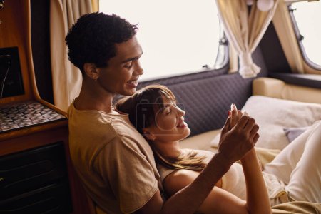 Ein Mann und eine Frau verschiedener Rassen liegen friedlich zusammen auf einem Bett in einer gemütlichen Umgebung und genießen einen romantischen Moment während ihres Kurzurlaubs.