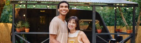 Téléchargez les photos : Un homme se tient à côté d'une femme, tenant un verre de vin dans un moment romantique pendant leur escapade en couple interracial. - en image libre de droit
