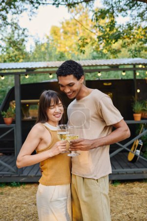 A man and a woman, an interracial couple, embrace while holding glasses of wine in a romantic gesture.