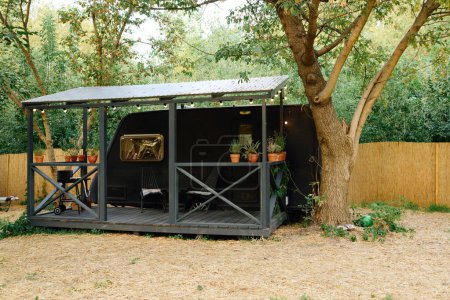 Un petit hangar avec une table confortable et des chaises sous un arbre feuillu, offrant un endroit paisible et serein pour la détente.