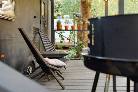 Téléchargez les photos : Terrasse avec un camping-car, barbecue et chaises, une escapade romantique dans la nature. - en image libre de droit