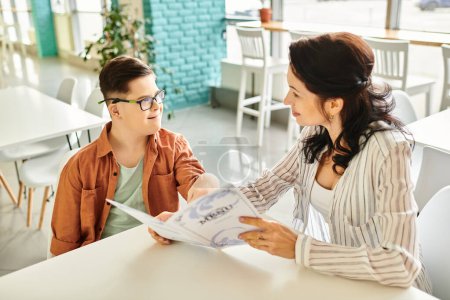 Photo for Loving mother sitting in cafe with her son with Down syndrome with glasses and menu, inclusive - Royalty Free Image