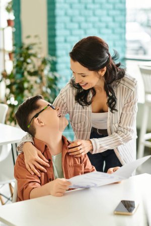 Photo for Joyful good looking mother in casual clothes with her inclusive son with Down syndrome holding menu - Royalty Free Image