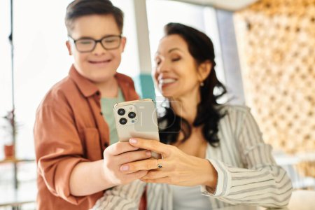 Foto de Centrarse en el teléfono inteligente moderno en manos de madre alegre borrosa y su hijo inclusivo con síndrome de Down - Imagen libre de derechos