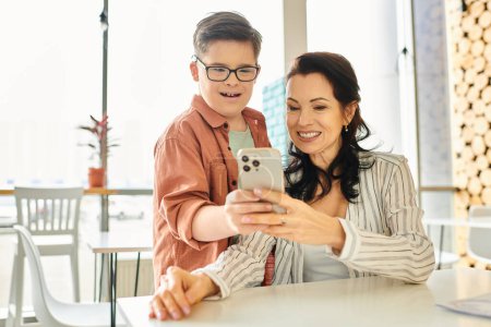 fröhlicher Junge mit Down-Syndrom, der Zeit mit seiner schönen Mutter im Café verbringt, Smartphone in der Hand