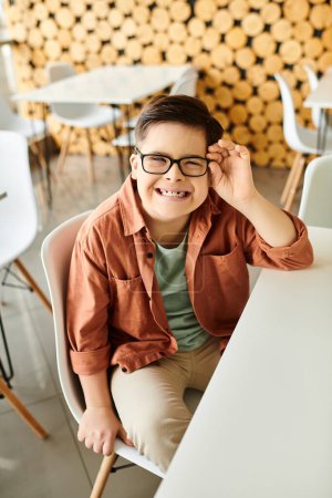 cheerful inclusive preteen boy with Down syndrome with glasses sitting in cafe and smiling at camera
