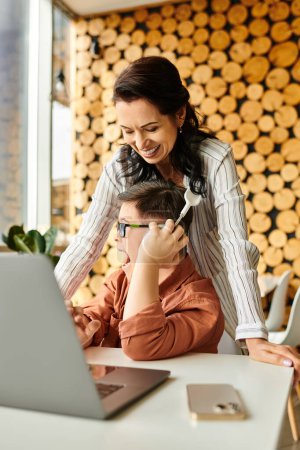 alegre madre pasar tiempo con su hijo con síndrome de Down en la cafetería mientras juega en el ordenador portátil