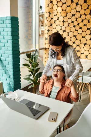 adorable inclusive boy with Down syndrome spending time with his merry mother in front of laptop