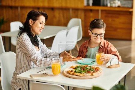 attrayant mère manger de la pizza et boire du jus avec son fils mignon inclusif avec trisomie 21
