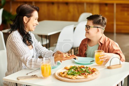 Téléchargez les photos : Attrayant mère manger de la pizza et boire du jus avec son fils mignon inclusif avec trisomie 21 - en image libre de droit