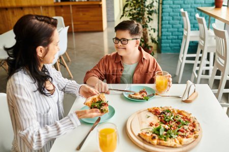 Photo for Cheerful mother eating pizza and drinking juice with her inclusive cute son with Down syndrome - Royalty Free Image