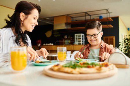 mère positive manger de la pizza et boire du jus avec son fils mignon inclusif avec trisomie 21