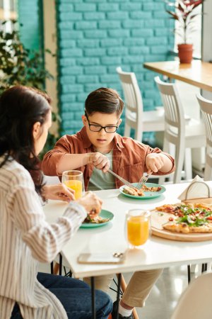 Photo for Positive mother eating pizza and drinking juice with her inclusive cute son with Down syndrome - Royalty Free Image