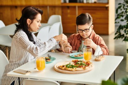 Téléchargez les photos : Mère joyeuse manger de la pizza et boire du jus avec son fils mignon inclusif avec trisomie 21 - en image libre de droit