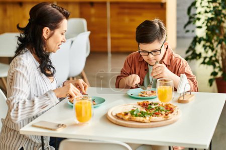Photo for Jolly mother eating pizza and drinking juice with her inclusive cute son with Down syndrome - Royalty Free Image