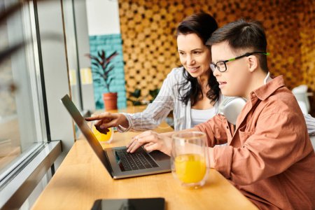 Photo for Joyful inclusive boy with Down syndrome with headphones playing on laptop near his mother in cafe - Royalty Free Image