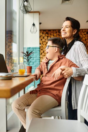 Téléchargez les photos : Joyeuse mère passer du temps avec son fils inclusif avec le syndrome de Down devant un ordinateur portable dans un café - en image libre de droit