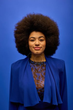 A fashionable African American woman stands confidently in front of a vibrant blue background.