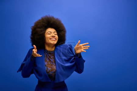 Foto de Elegante mujer afroamericana con cabellos rizadosposa contra el fondo azul vibrante. - Imagen libre de derechos