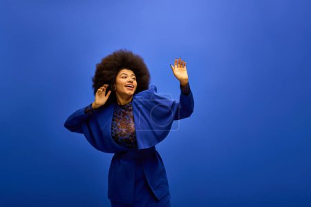 Trendy African American woman in a blue jacket raises her hands gracefully.