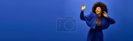 Foto de Elegante mujer afroamericana en vestido azul de moda sostiene las manos contra el vibrante telón de fondo. - Imagen libre de derechos
