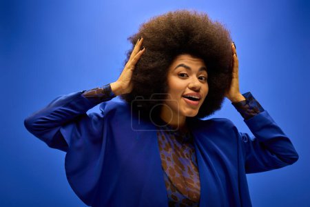 Mujer afroamericana con estilo en traje de moda, sosteniendo y admirando su voluminoso pelo afro.