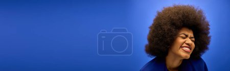 A stylish African American woman with curly hairdosmiles for the camera against a vibrant backdrop.