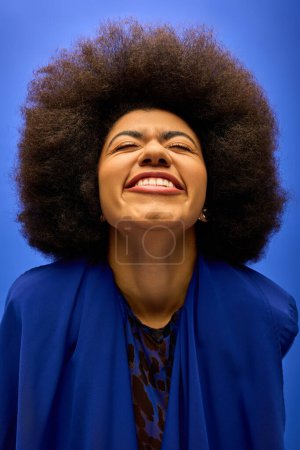 Téléchargez les photos : Femme afro-américaine élégante avec des cheveux bouclés souriant dans une veste bleue à la mode. - en image libre de droit