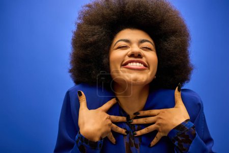 Foto de Elegante mujer afroamericana sonríe, cogida de la mano en el pecho. - Imagen libre de derechos