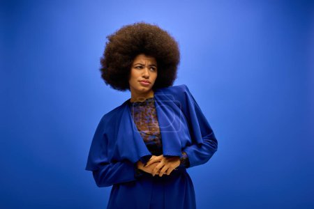 Trendy African American woman with curly hairdo poses in front of vivid blue backdrop.