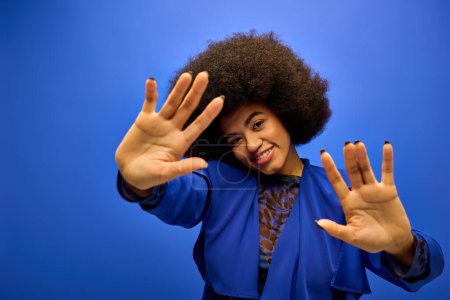 Elegante mujer afroamericana con el pelo rizado en traje de moda, levantando alegremente sus manos.