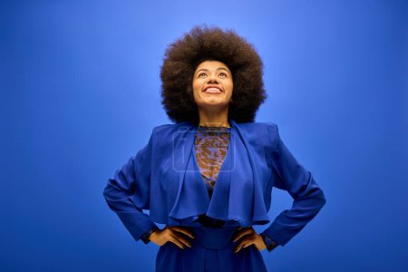 African American woman with curly hairdostanding stylishly against vibrant blue backdrop.