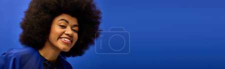Una elegante mujer afroamericana con un afro voluminoso posa sobre un vibrante telón de fondo.