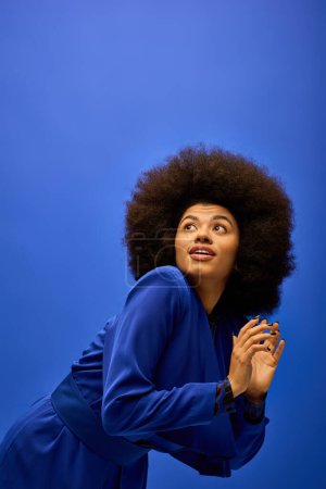 Fashionable African American woman in trendy attire and afro hairstyle, posing confidently in front of a bright blue backdrop.