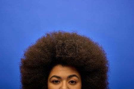 Elegante mujer afroamericana con el pelo rizado vibrante telón de fondo azul.