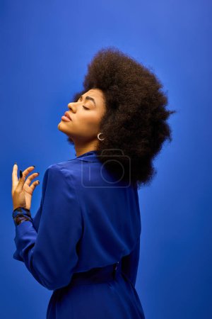 Téléchargez les photos : Une femme afro-américaine à la mode avec une coiffure bouclée pose dans une robe bleue sur un fond coloré. - en image libre de droit