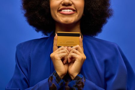 Stylish African American woman in trendy attire holding credit card to her face.